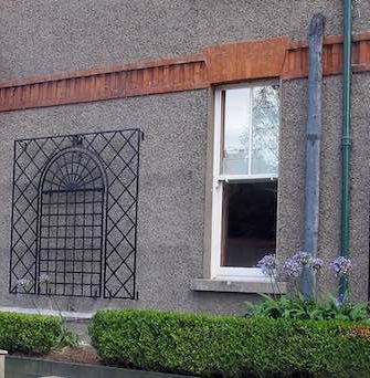 Treillage Metal Wall Trellises installed between the windows of a house with a grey façade