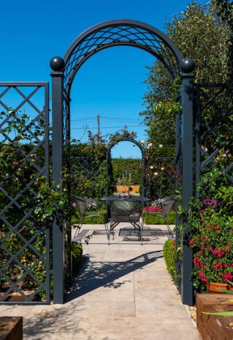 The Portofino Romanesque Garden Arch and Paravent Metal Railing Panel by Classic Garden Elements in a patio area