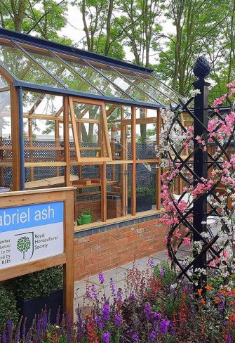 The Charleston Rose Obelisk by Classic Garden Elements in front of a Gabriel Ash greenhouse