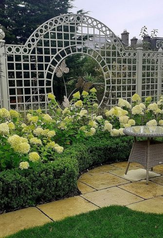 The Trianon Rose Treillage Set by Classic Garden Elements behind a border of hydrangeas and a box hedge