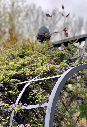 Close-up of the arch and pine-cone finials of the Victorian Rose Arbour by Classic Garden Elements, seen here covered in clematis