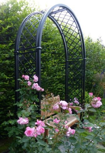 The Portofino Romanesque Garden Arch with a wooden bench and pink roses