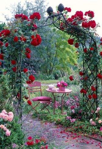 Table and chair set up beneath a Classic Garden Elements rose arch covered in roses