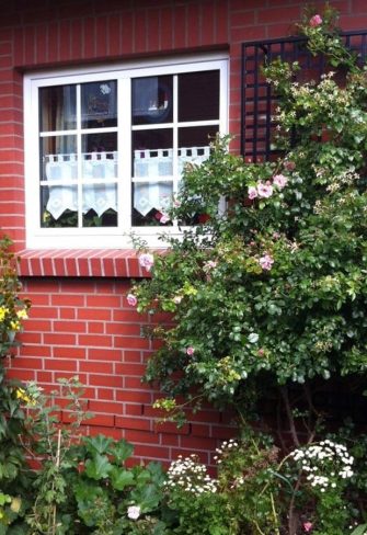 Two metal wall trellises by Classic Garden Elements on a brick house wall, covered in roses